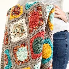 a woman is holding up a crocheted blanket