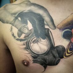 a man with a gas mask tattoo on his chest and hand reaching for something in front of him