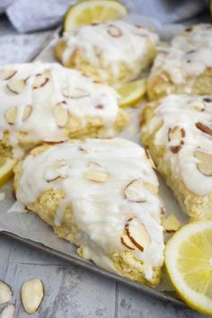 lemon almond scones with icing on a baking sheet next to sliced lemons