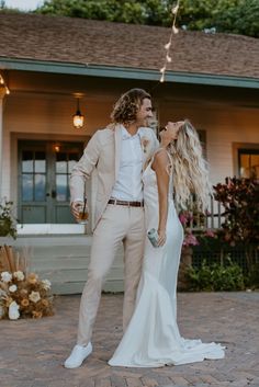 a bride and groom standing in front of a house with string lights hanging from the roof