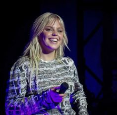 a woman holding a microphone in her right hand and smiling at the camera while standing on stage