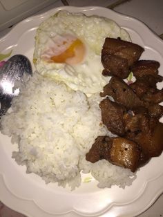 a white plate topped with rice and meat next to a fried egg on top of it