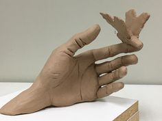 a clay hand is on top of a piece of cardboard that has been placed in front of it