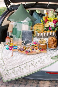 a trunk filled with food and drinks on top of a white cloth covered table in the back of a car