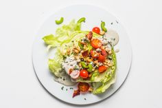 a white plate topped with lettuce, tomatoes and dressing on top of it