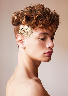 a young man with curly hair wearing a gold brooch