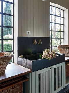 a kitchen with two sinks and baskets on the counter top next to windows that look out onto trees