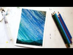 some colored pencils sitting on top of a table next to an art project with watercolor