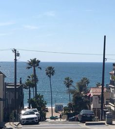 cars parked on the side of an empty street next to the ocean and palm trees