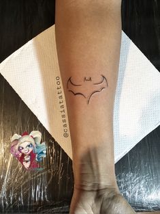 a woman's arm with a tattoo that has a batman symbol on the wrist