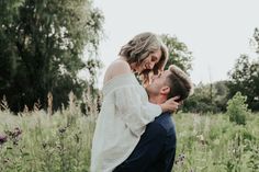 a man holding a woman in his arms while they are standing in the middle of a field