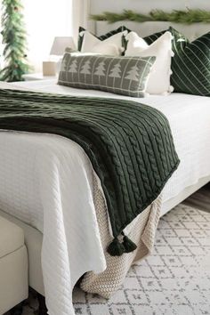 a white bed topped with green and white pillows next to a window covered in christmas trees