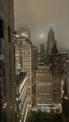 the city skyline is lit up at night, with skyscrapers in the background and foggy skies