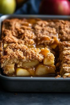 a close up of a pie in a pan with apples and other fruit behind it