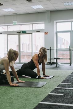 two women doing push ups on yoga mats in an airport gym area with windows looking out onto the city