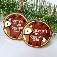 two personalized christmas ornaments hanging from a tree branch with pine branches in the background