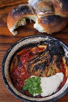 a bowl filled with food sitting on top of a table next to a baguette