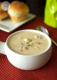 a white bowl filled with soup on top of a red place mat next to rolls