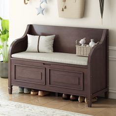 a wooden bench with drawers underneath it in front of a potted plant and wall hangings