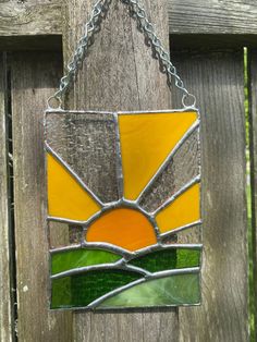 a stained glass sun catcher hanging on a wooden fence with chains attached to the chain