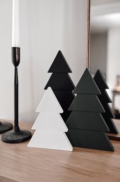 three black and white christmas trees sitting on top of a wooden table next to a candle