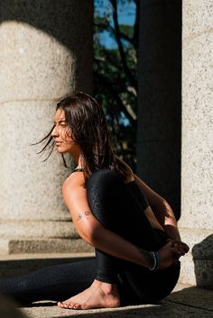 a woman sitting on the ground with her hands behind her back as she looks off into the distance