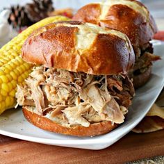 two pulled pork sandwiches on a plate with corn on the cob next to it