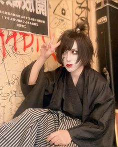 a woman with black and white makeup is sitting on the floor in front of a wall