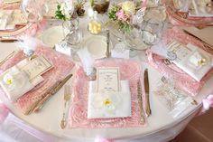 the table is set with pink and white linens, silverware, and napkins