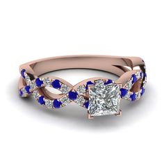 a princess cut diamond ring with blue sapphire stones on the band and side stones in 18k rose gold