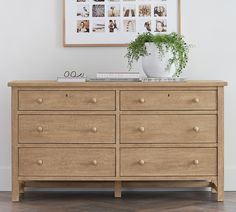 a wooden dresser sitting in front of a wall with pictures on it and a potted plant