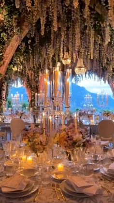 a table set up for a formal dinner with candles and flowers hanging from the ceiling