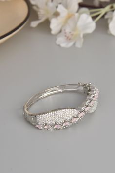 Embrace the soft elegance of our Blush Bloom Bracelet, a delicate ode to feminine beauty. Crafted from durable brass and adorned with shimmering CZ stones, this bracelet captures the essence of grace and sophistication. Finished in radiant rhodium, the gentle pink CZ stones evoke the tender bloom of spring flowers, infusing your look with a touch of natural charm. Each stone radiates with a subtle sparkle, casting a luminous glow that captivates the senses. Let this exquisite bracelet grace your Elegant Adjustable Stones Bangle, Elegant Adjustable Bangle With Stones, Formal Pink Bracelets With Diamond Accents, Elegant White Gold Bracelets With Stones, Elegant White Gold Bracelet With Stones, Silver Bangle Bracelet With Elegant Design, Hand Set Elegant Crystal Bracelet, Pink Hand-set Bangle Jewelry, Elegant Pink Diamond Bracelet With Diamond Accents