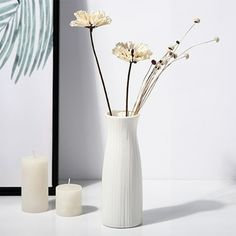 three flowers in a white vase next to two candles