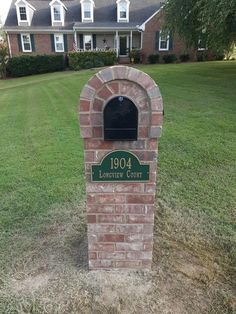 a brick mailbox sitting in the middle of a field next to a large house