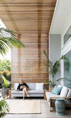 a woman sitting on top of a white couch in a living room next to a palm tree