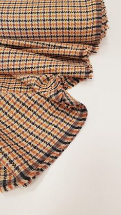 an orange and black checkered scarf laying on top of a white surface with the fabric pulled back