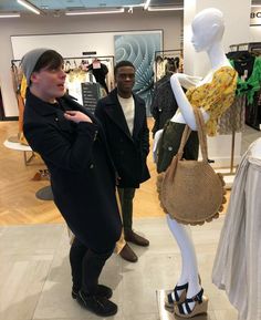 two men standing next to a mannequin holding a purse in front of them