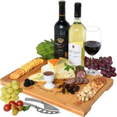 a wooden cutting board topped with cheese, crackers and bottles of wine next to grapes