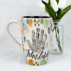 a coffee mug with a hand print on it next to a vase filled with tulips