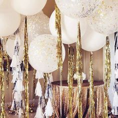 balloons and streamers are hanging from the ceiling in front of a wall with gold confetti