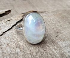 An elegant crystal white large oval Rainbow Moonstone has been set in sterling silver with a handmade ring band from sterling silver half dome wire. This moonstone is pearly white and shines on its own with hues of pink, blue, and even orange. The luminescent quality of the moonstone makes this ring beautifully unique and elegant. The stone is 13mm x 18mm in size with varying heights depending on the chosen stone. This is a closed setting-the back is not open. The stone sits in a solid sterling Oval Large Stone Moonstone Wedding Ring, White Moonstone Opal Ring In Oval Cabochon Shape, Large Oval Moonstone Ring, White Oval Moonstone Ring Gift, White Opal Ring With Oval Cabochon Shape, Oval White Moonstone Ring For Gift, Oval Moonstone Ring With Large Stone In Sterling Silver, White Moonstone Ring With Oval Cabochon, Large Oval White Moonstone Ring