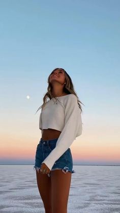 a woman standing on top of a beach next to the ocean wearing high waist denim shorts