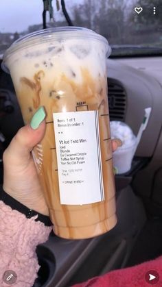 a woman holding up a cup of iced coffee in her car with the driver's seat behind her