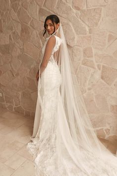 a woman in a wedding dress standing next to a stone wall wearing a long veil