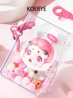 a pink and white kitty doll in a clear box with some pom poms