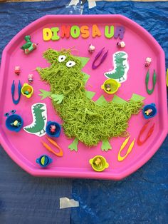 a pink tray with green grass and scissors on it that says dinosaur in the center