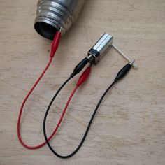 two wires connected to an electric device on top of a wooden table next to a metal can