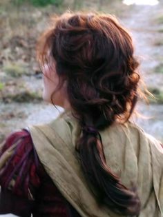 a woman with long hair wearing a brown and red dress standing in front of a river