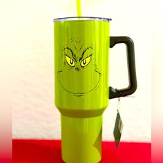 a green mug with an angry grin face drawn on the side and a yellow straw sticking out of it